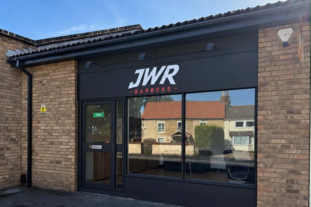 The JWR Barbers shopfront on Main Road, Washingborough — black fascia under a pitched roof, the village cottages reflected in the window